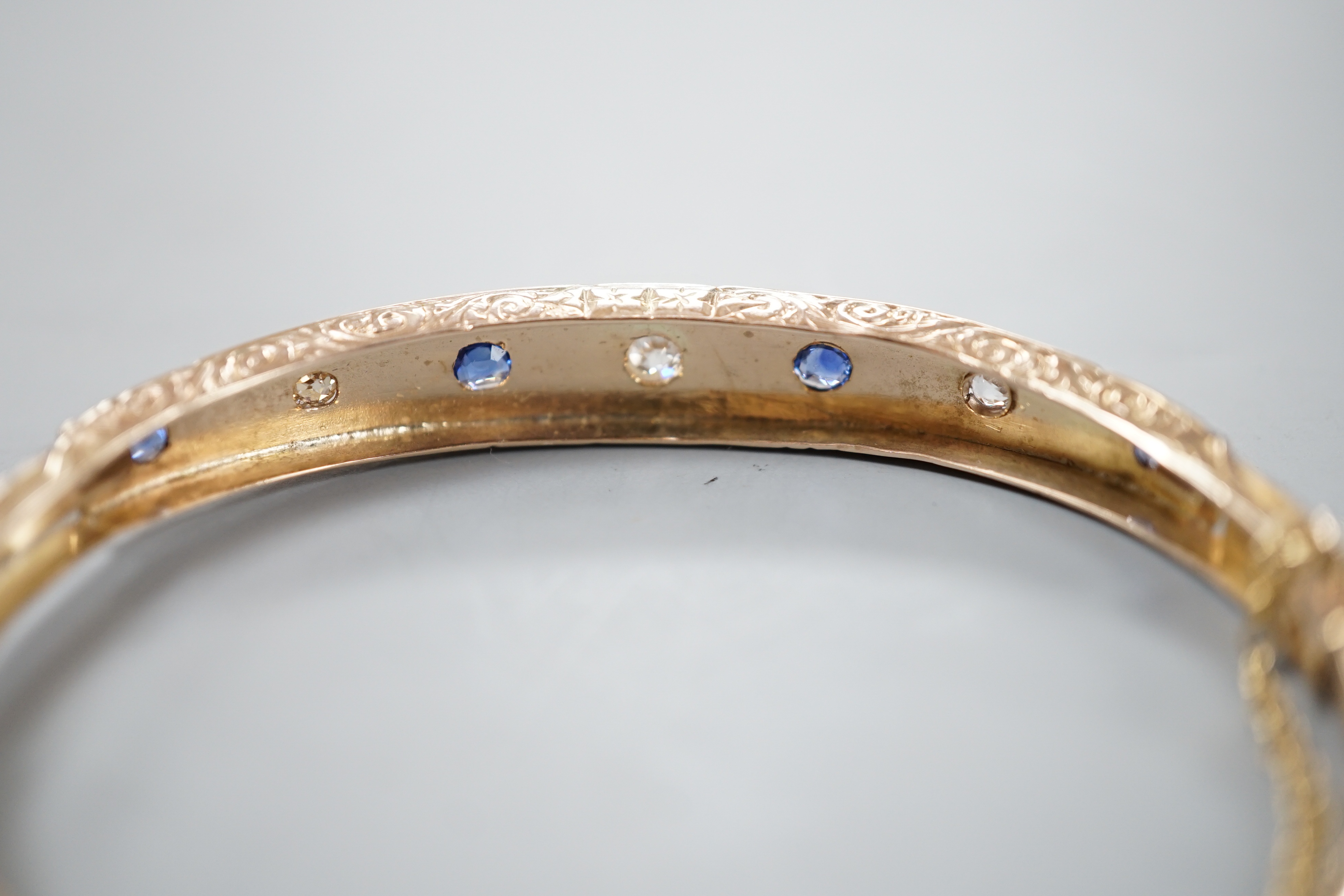 A late Victorian engraved yellow metal, four stone sapphire and three stone diamond set hinged bangle, gross 10.5 grams.